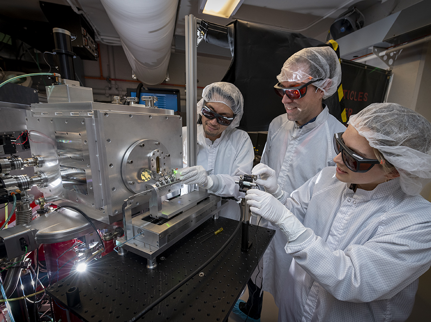 Three people in cleanroom PPE working on a machine