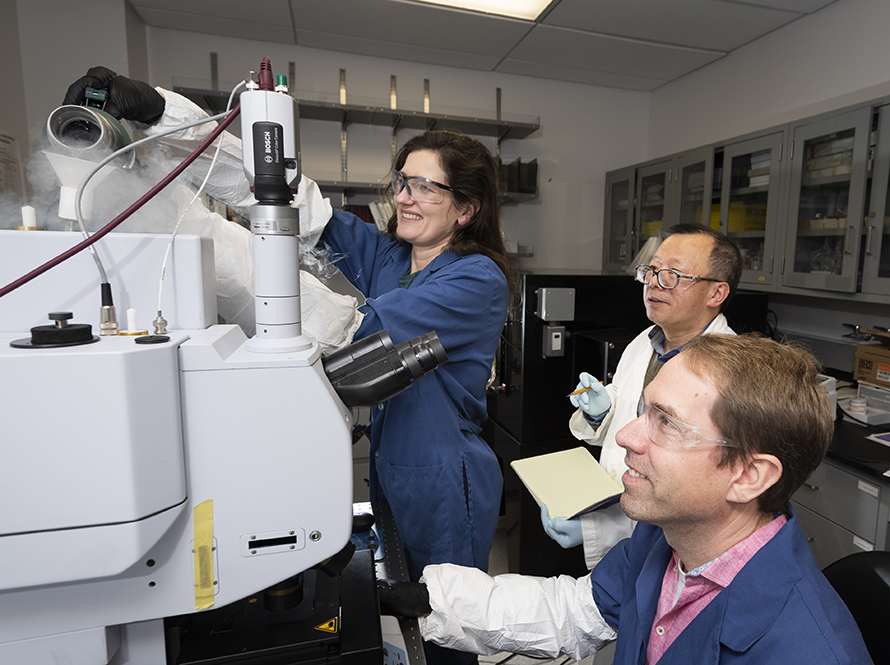 Two researchers in PPE operate a machine while a third looks on