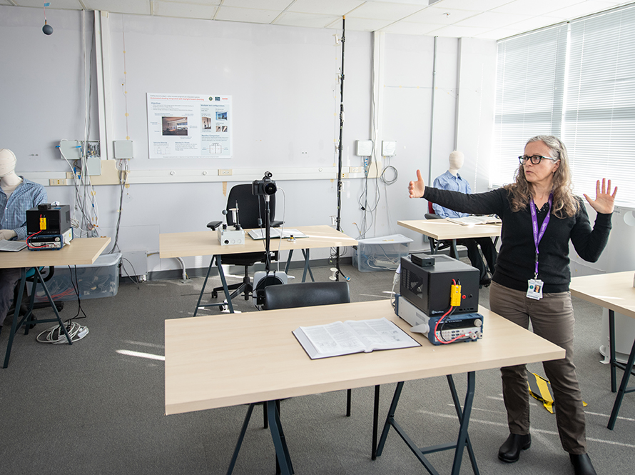 A person standing next to one of several desks in open floor plan lab setting